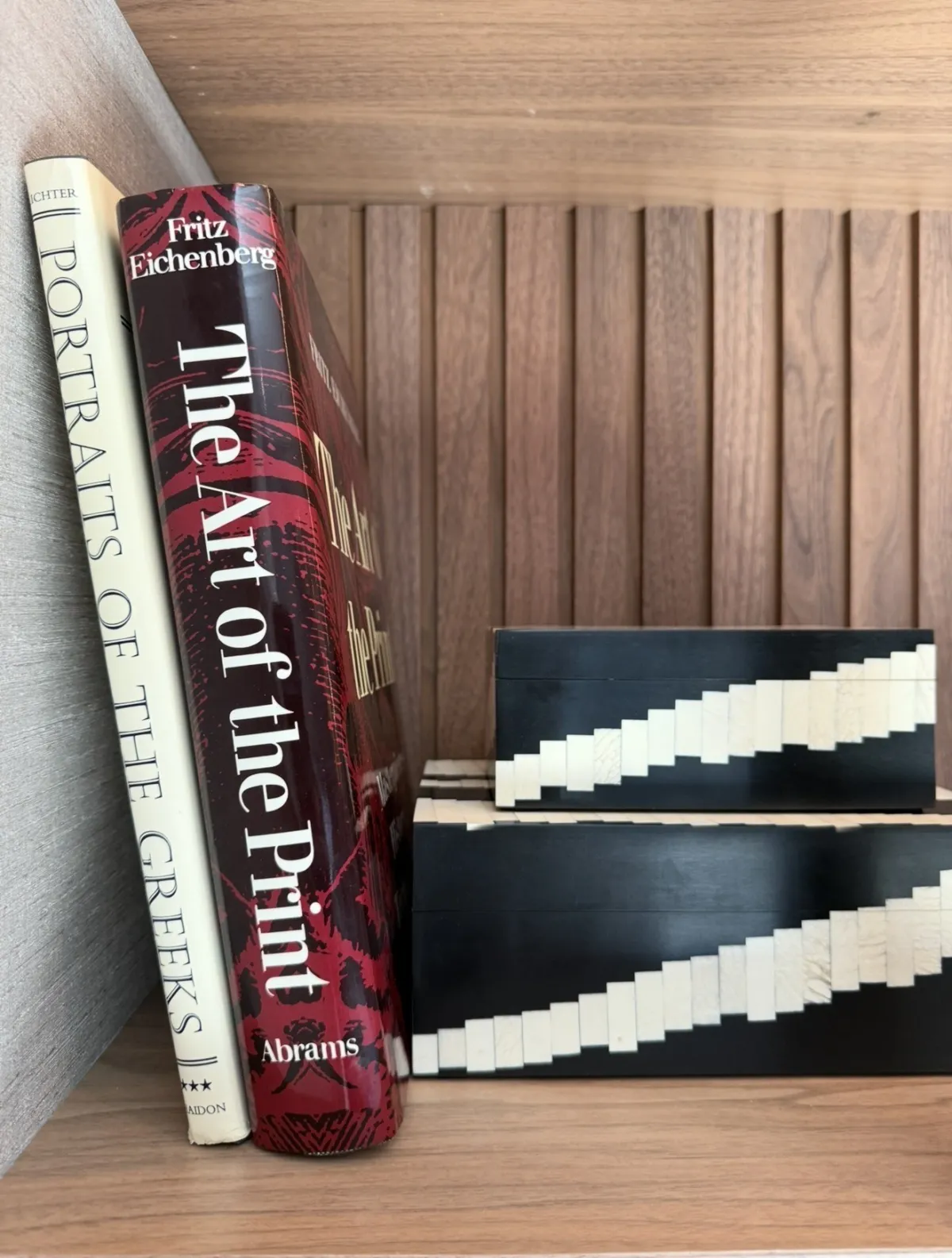 Art books and black patterned boxes on a wood shelf