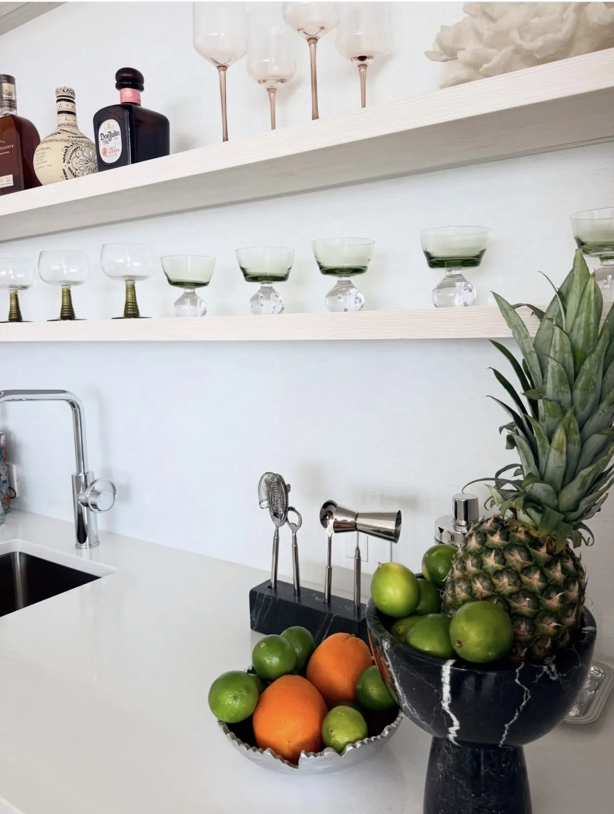 White bar shelves with glassware above a styled counter of citrus and pineapple