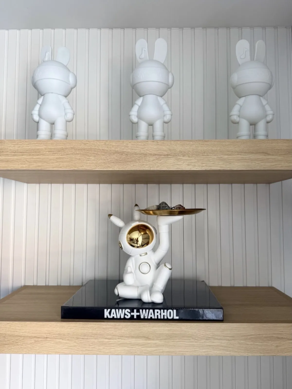 White sculptural figures and a gold accented sculpture displayed on wood shelves