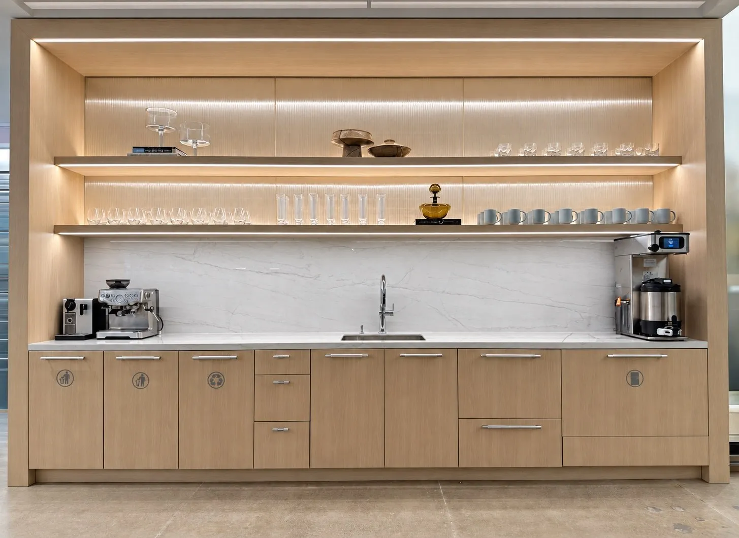 Wide view of a corporate café bar with illuminated shelves, glassware, mugs, and a coffee station