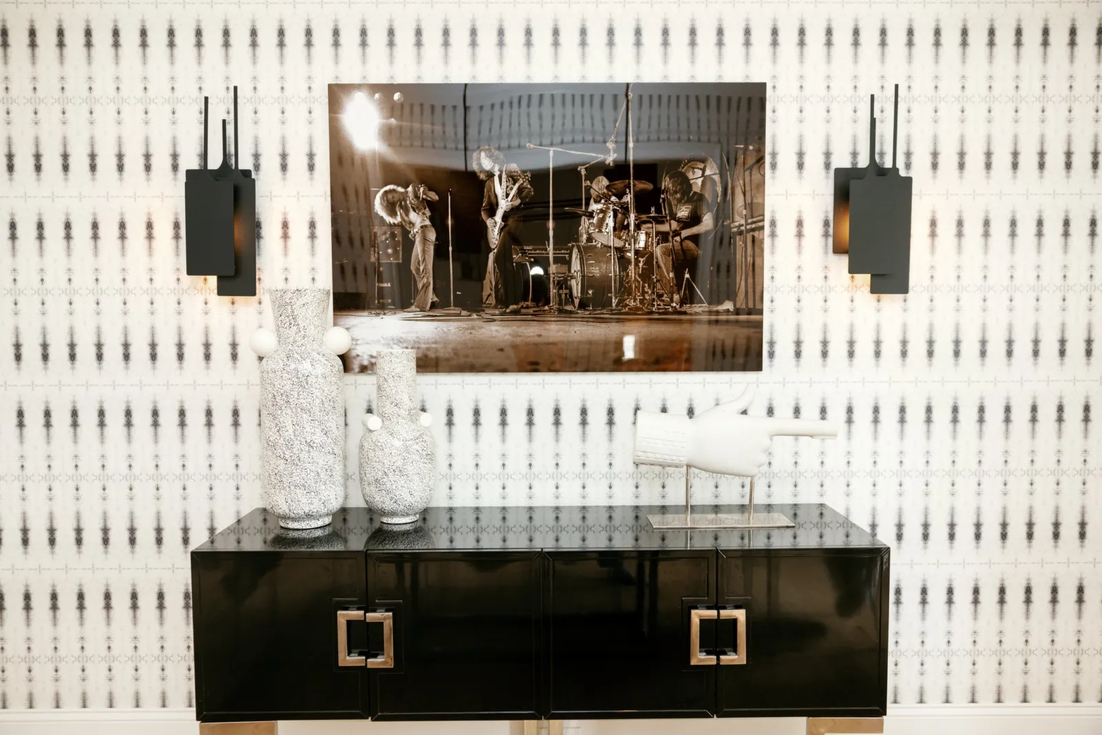 Black lacquer console beneath a framed photograph against patterned wallpaper