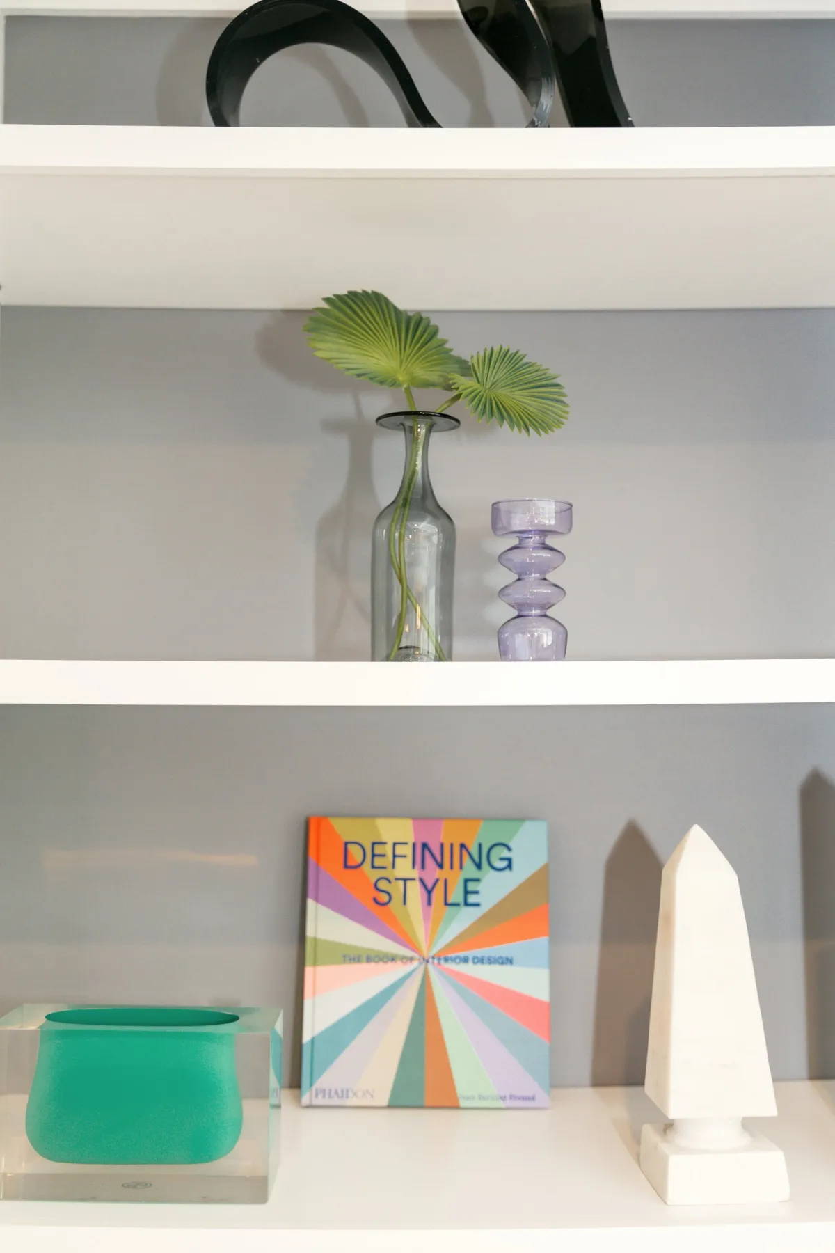 Palm leaf, a Defining Style book and a white obelisk on built-in shelves
