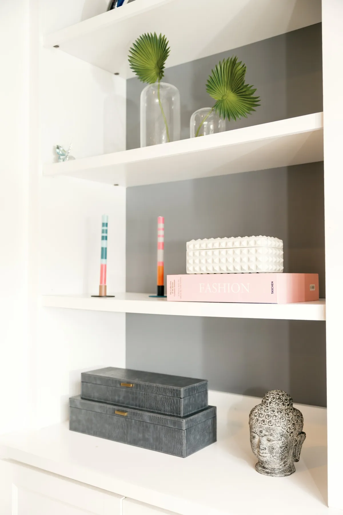 Built-in shelves with glass vases, palm leaves and gray storage boxes