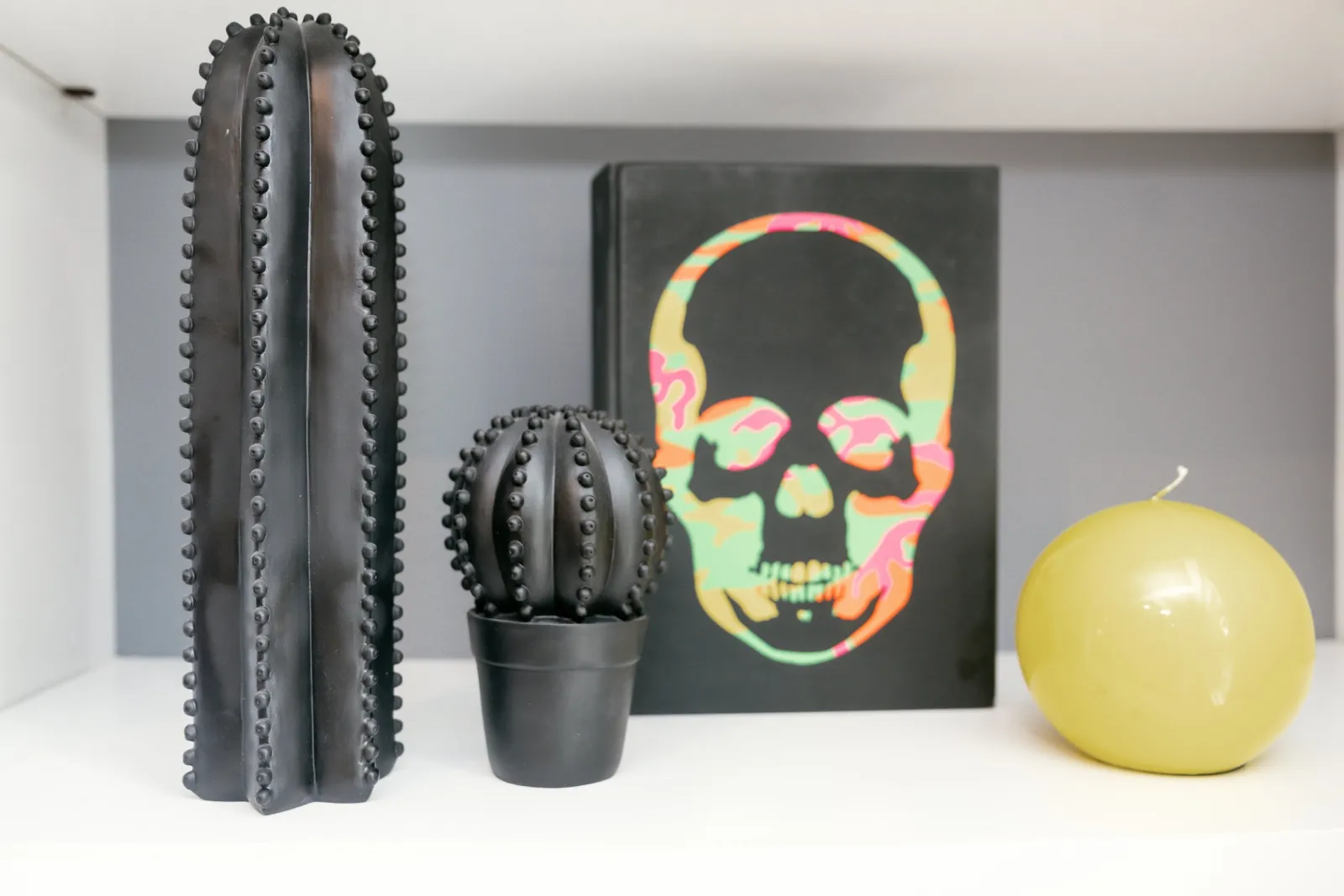 Black cactus sculptures, skull artwork and a yellow candle on a shelf