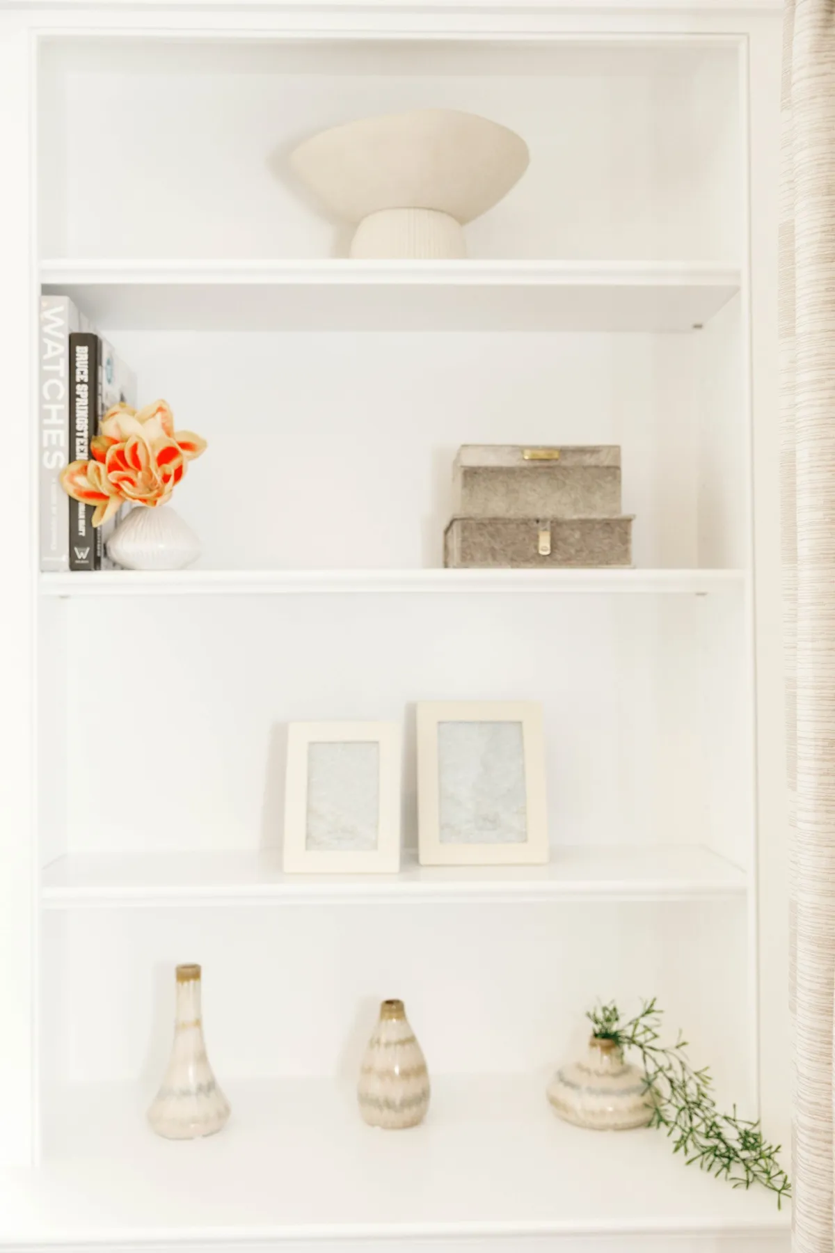 Close view of styling on white built-in shelves with orange flowers and books
