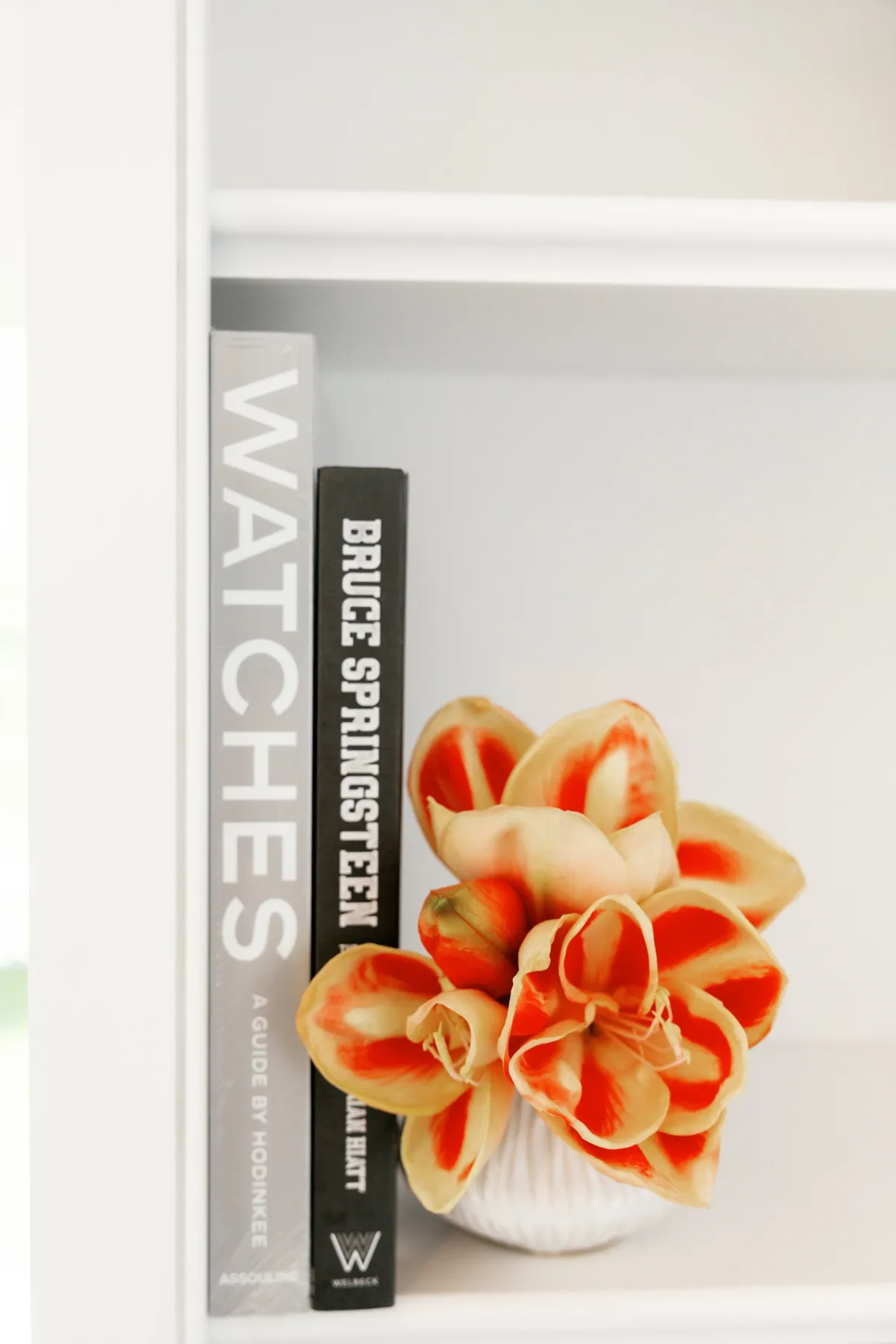 Orange flowers beside art and watch books on white shelving