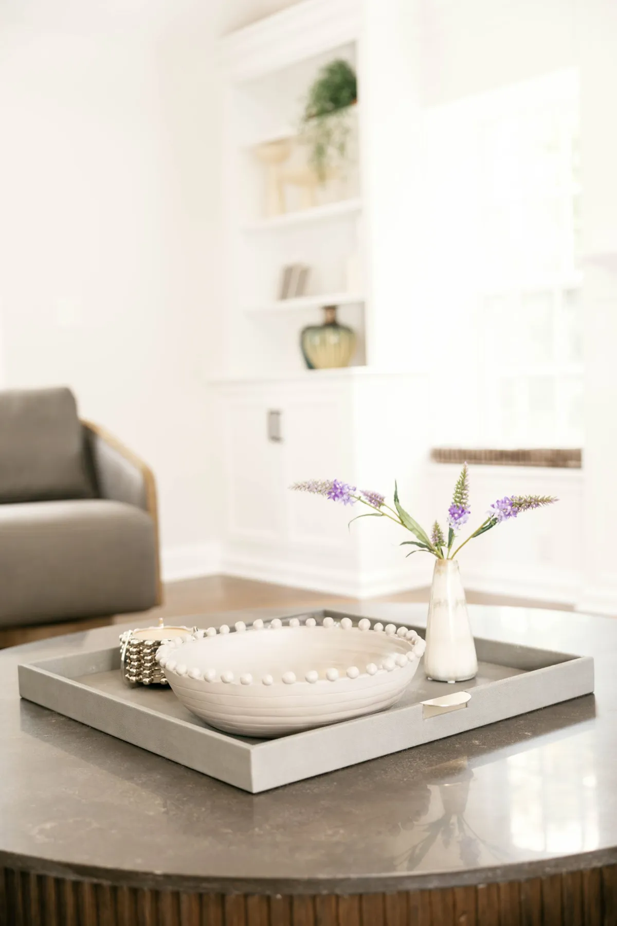Tray, sculptural white bowl, and purple flowers on a coffee table