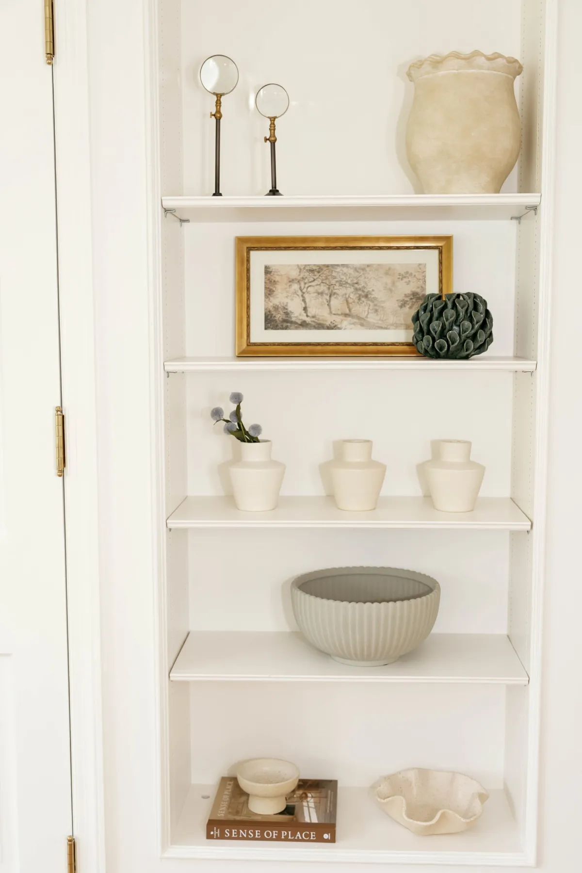 Styled built-in shelves with framed art, ceramic vessels, and a ribbed bowl