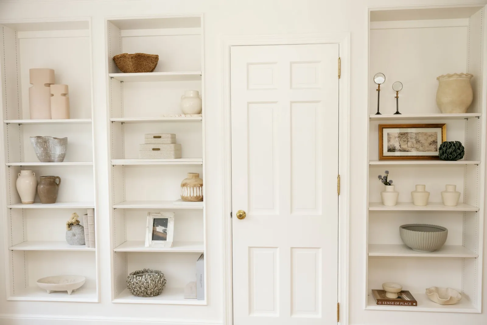 White built-in shelves styled with neutral ceramics and artwork around a doorway