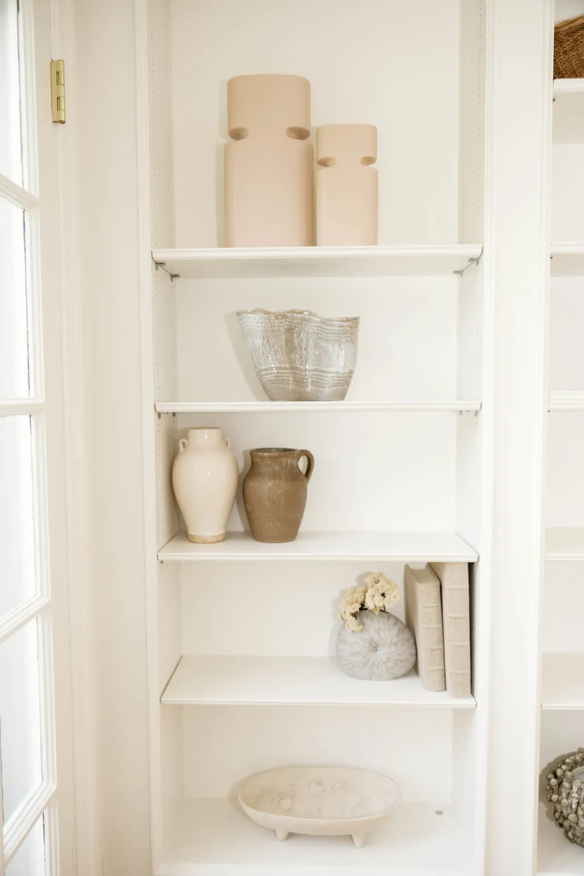 Ceramic vessels and textured bowls arranged on white built-in shelves