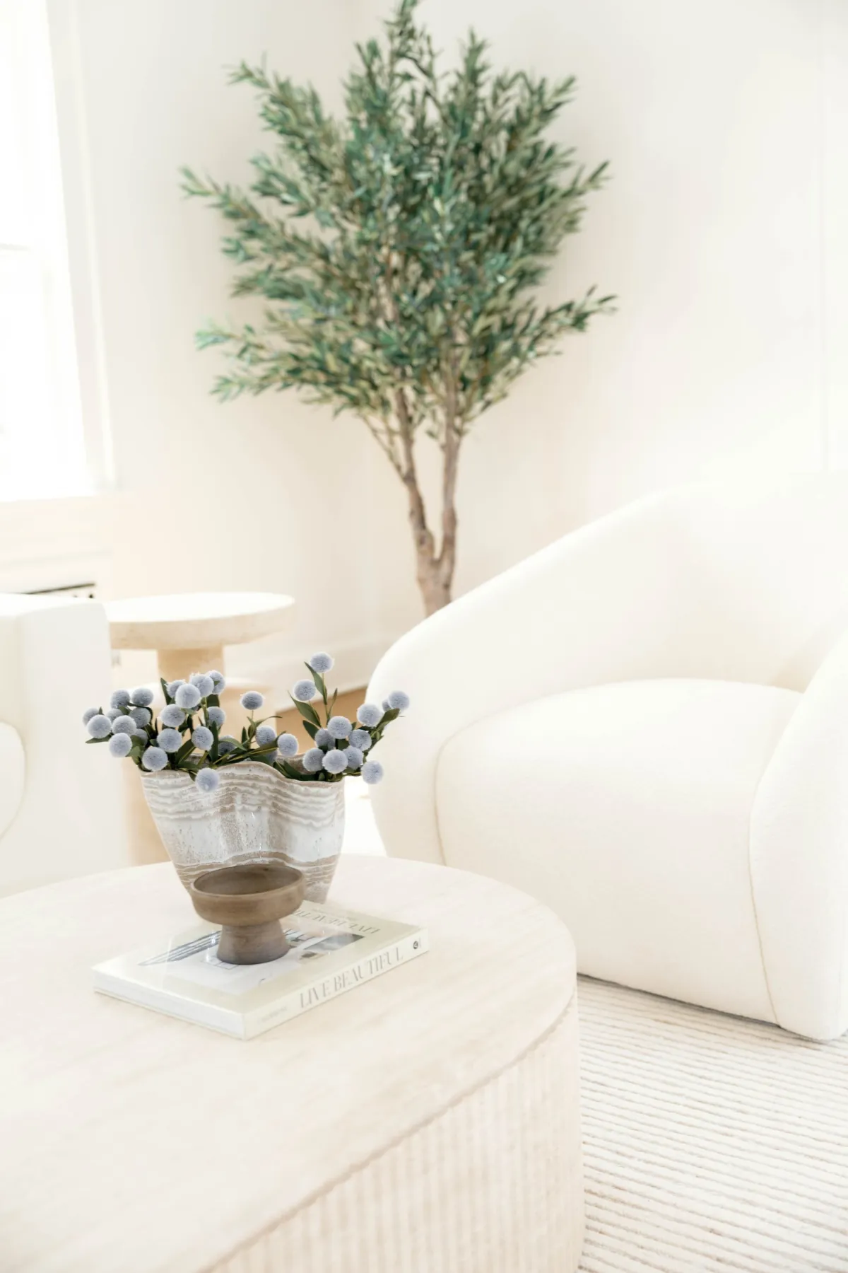 Soft blue flowers and sculptural bowl on a coffee table beside a curved chair