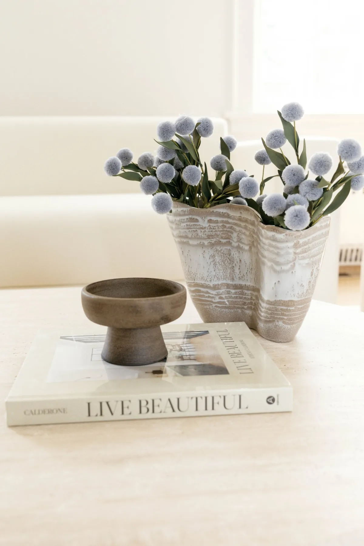 Blue flowers and a small bowl styled over a Live Beautiful book