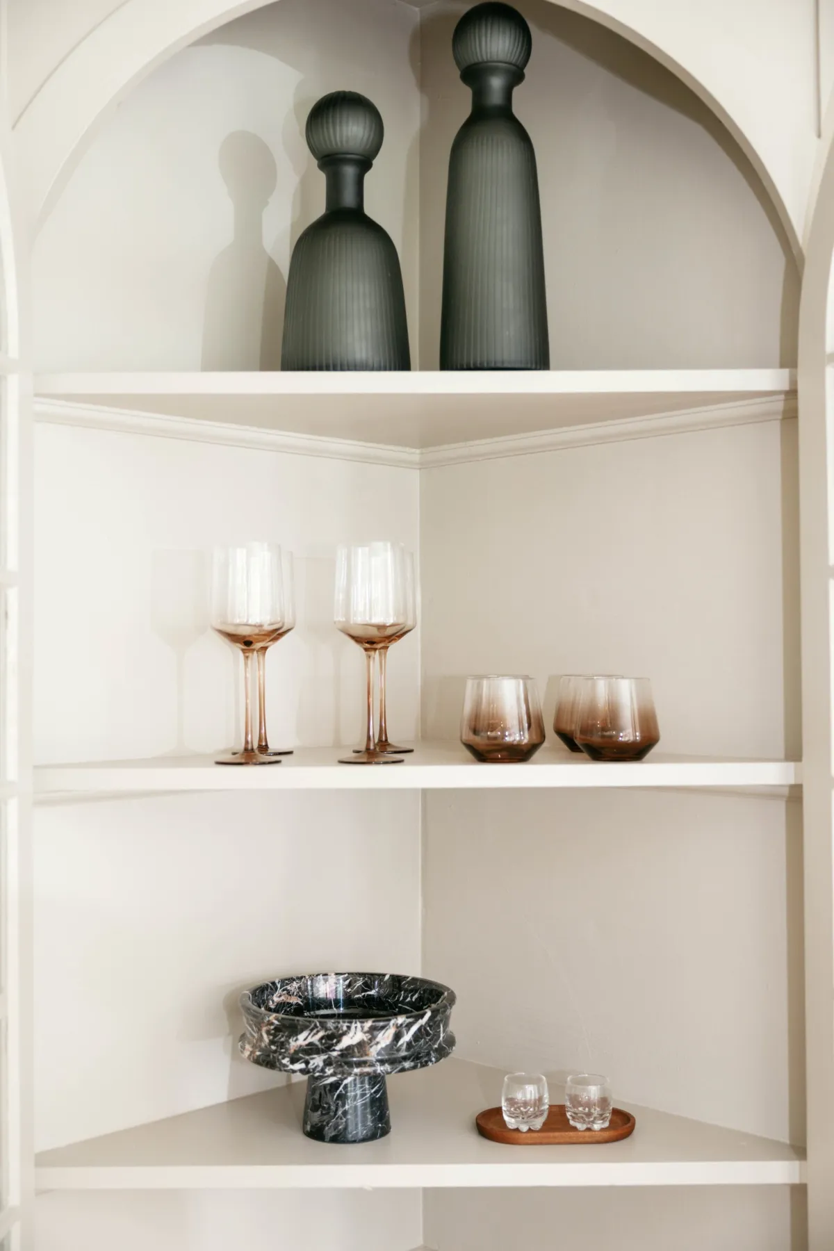Arched bar shelves with charcoal vessels, rose glassware, and marble bowl