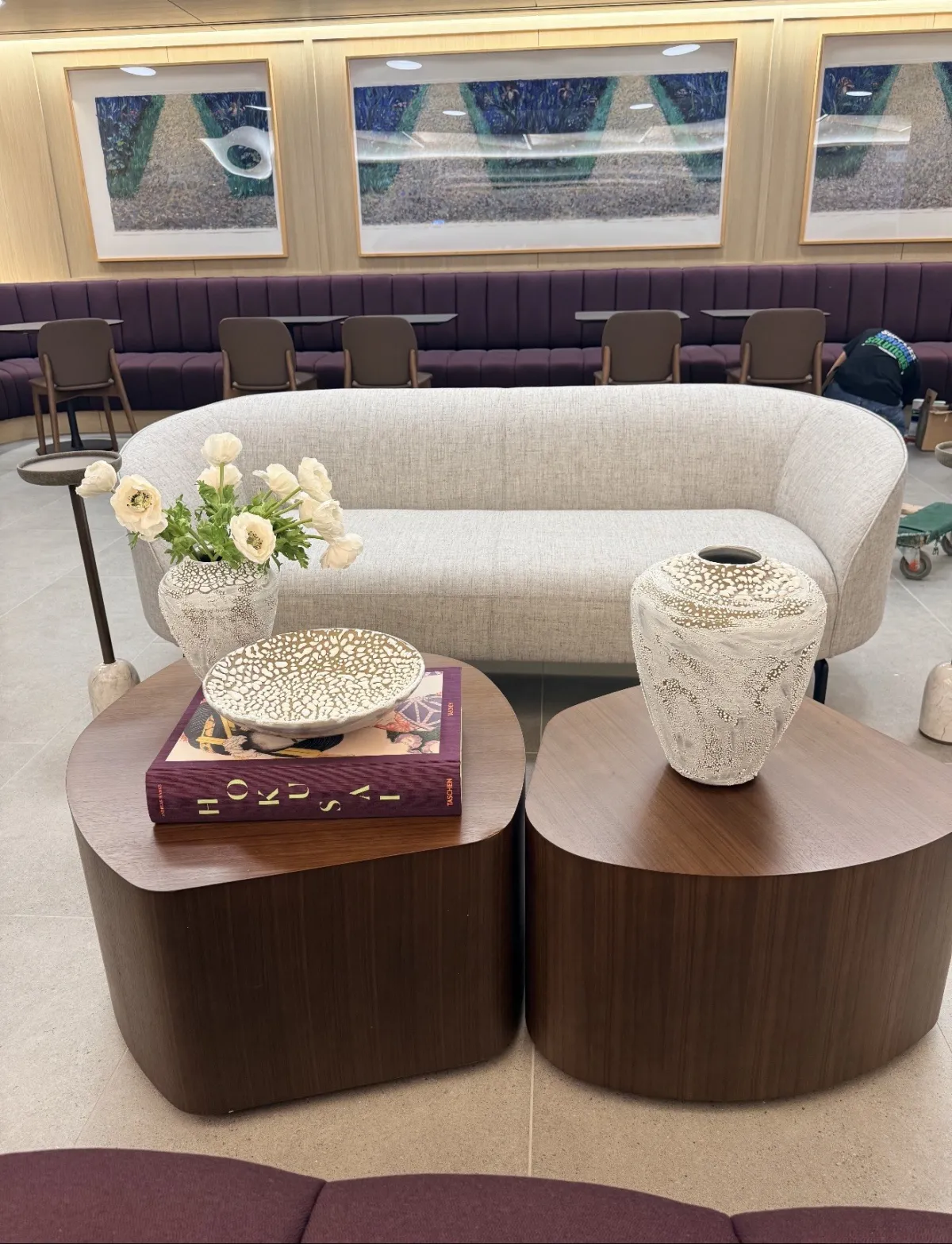 Workplace lounge with a curved sofa and walnut drum tables styled with a vase and art books