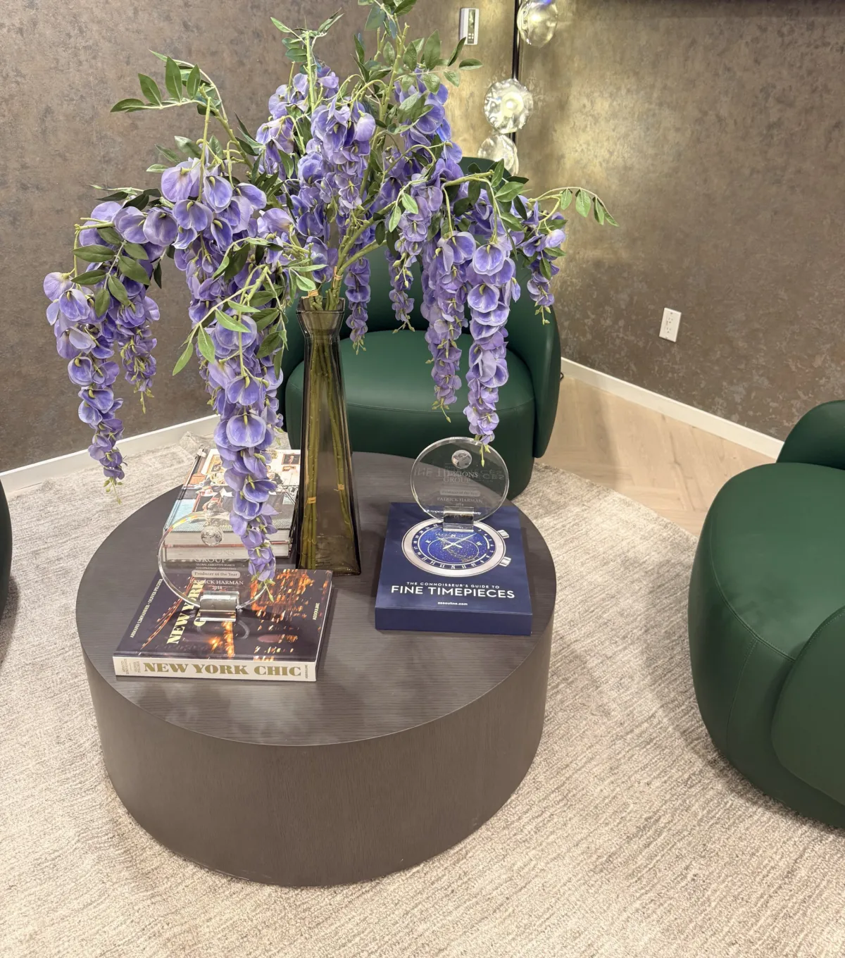 Wisteria arrangement on a round table with art books between green lounge chairs